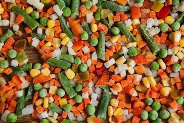Closeup colorful frozen vegetables on cutting board in cutting process. Carrot, corn, pepper, onion and asparagus in mess