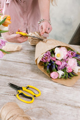 Woman make tulip bouquet in flower shop.Young florist make festive floristry assemble in workshop on wooden background