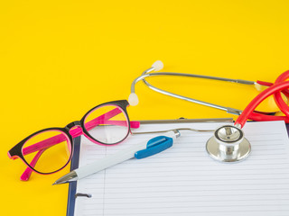 Stethoscope with clipboard, pen and glasses on yellow background for Doctor working in hospital writing a prescription, Healthcare and medical concept