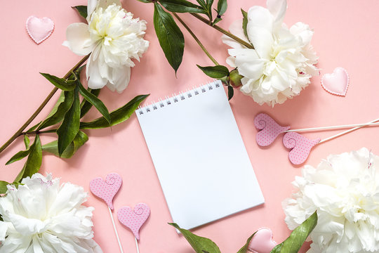 Blank open notepad with white peonies on a pink background. Place for a message, top view.