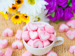 Closeup of sweet marshmallow in the shape of heart on wooden plate and flower at background. Concept about love and relationship. (Soft Style for Background)