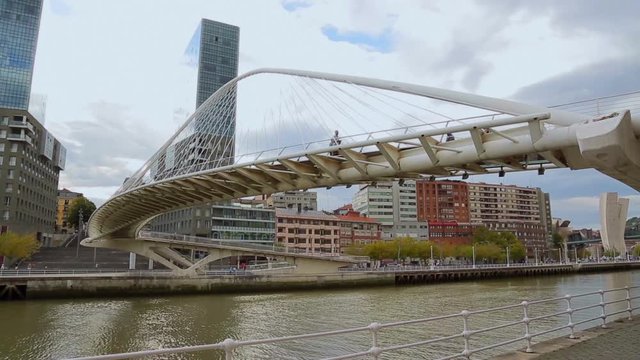 River with footbridge across, shown against city skyline, people along walkway