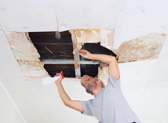 man cleaning mold on ceiling.Ceiling panels damaged huge hole in roof from rainwater leakage.Water...