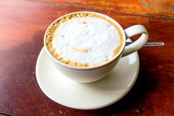 Hot cappuccino in white cup on wood table.