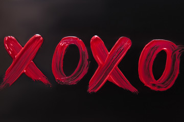 Inscription lipstick hugs and kisses on black backdrop. Cosmetic handwriting abbreviation,...