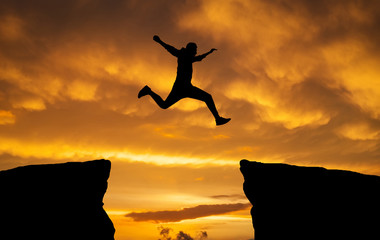 Man jumping over rocks with gap on sunset fiery background. Element of design.
