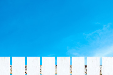 White picket fence and soft white clouds against blue sky.