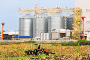 Agricultural Silos - Building Exterior, Storage and drying of grains, wheat, corn, soy, sunflower against the blue sky with farm tractors in the foreground.