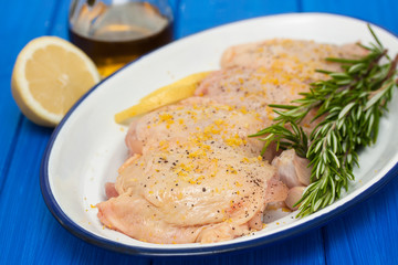 raw chicken with lemon and rosemary on white dish