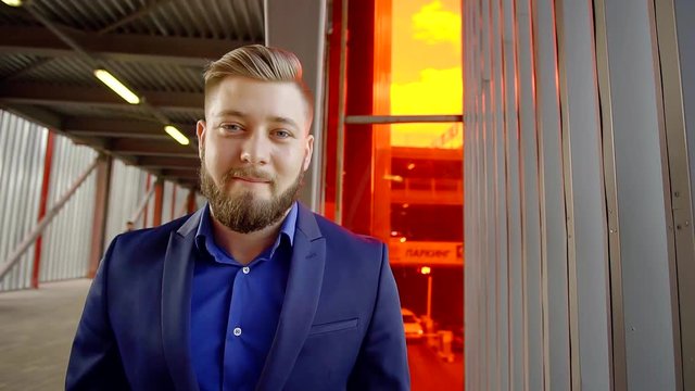 sports is a brutal man with big shoulders and a beard in a blue suit standing in the tunnel between Parking and office. portrait of a stylish business person.