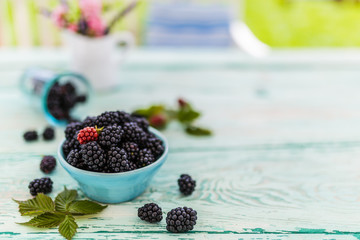 Fresh blackberries in bowl on wooden table in the garden.