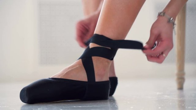 close up view woman put on black pointe ballet footwear to warm up and do workout exercises and practice ballet dance in studio