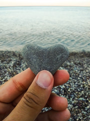 Hand holding a heart shaped stone at the beach