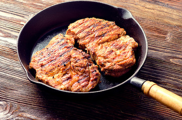 Roasted steaks in  pan on a dark wooden table.