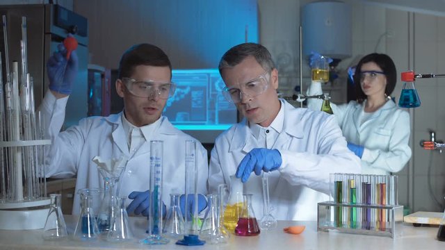 Technologists or scientist working in a chemical laboratory doing experiments with colorful solutions in beakers with two men working as a team in the foreground