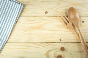 Tablecloth, wooden spoon, fork on wood table background.