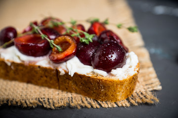 Bread with ricotta cheese and cherries on the wooden background. Shallow depth of field.