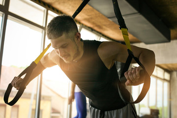 Young man workout in healthy club. Man doing exercise with strip  system.