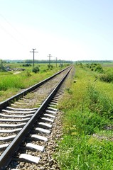 Fototapeta na wymiar Railroad tracks that run off into the distance among green grass on summer sunny day