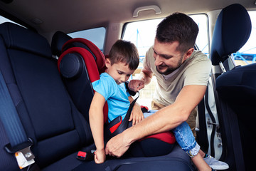 Concentrated father helps his son to fasten belt on car seat