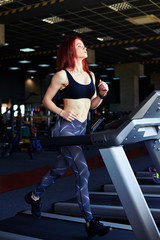 Pretty slim girl working out in a treadmill at the gym and smiling