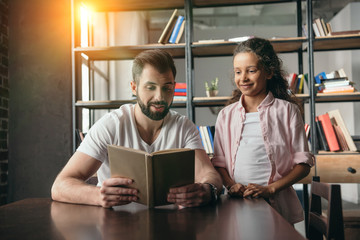 little african american girl reading book with her father at home