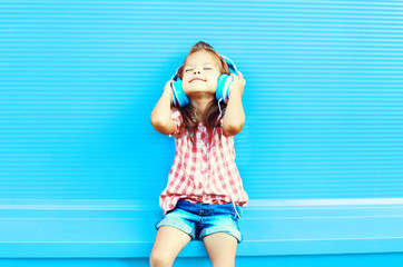 Happy little girl child listens to music in headphones on a colorful blue background
