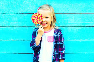 portrait happy smiling little girl child with a lollipop stick having fun over a blue background