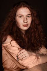 Naklejka premium pretty tender redhead girl with crossed arms posing in beige blouse, isolated on black