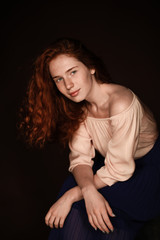 tender redhead woman posing in beige blouse for studio shot, isolated on black