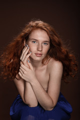tender beautiful redhead woman posing for studio shot, isolated on brown