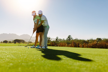 Male golf instructor teaching female golf player