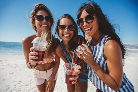 Three young women enjoying ice tea on seashore