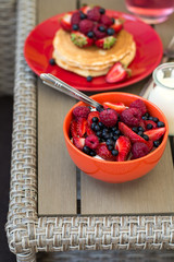 Healthy breakfast on garden furniture: cottage cheese with sour cream, strawberry, raspberry and blueberry, pancakes, yogurt and juice. Selective focus