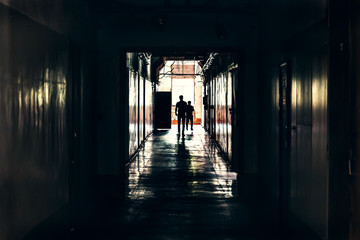 Dark corridor in building, doors and silhouettes of two man, perspective
