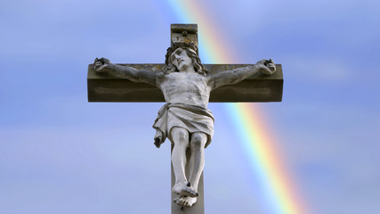 stone cross with Jesus and blue sky with rainbow