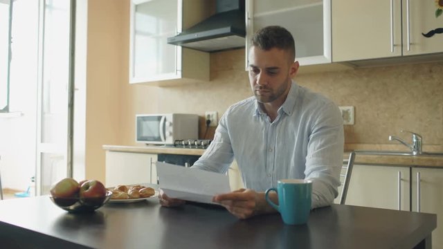 Uspet young man reading letter with unpaid bill in the kitchen at home