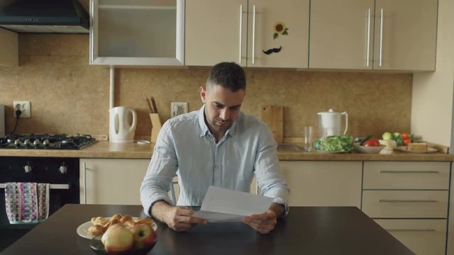 Uspet young man reading unpaid bills and hugged by his wife supporting him in the kitchen at home
