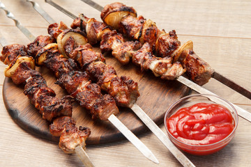 Grilled pork on skewers roasted on the grill on wooden chopping board with tomato sauce in a bowl