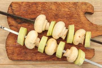 Zucchini and mushrooms on metal skewers on wooden chopping board