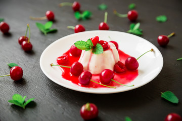 Panna cotta jelly with cherry in white plate on a dark table, tasty Italian dessert