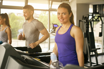 Fototapeta na wymiar Young man and women workout in gym. Friends together in gym on the treadmill. Woman looking at camera.