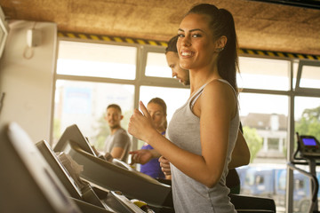 Young man and women workout in gym. Friends together in gym on the treadmill. Woman looking at camera.