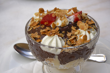 Chocolate profiterole pastry closeup served on a glass bowl with spoon.
Puff pastry with dark chocolate choux covered with whipped cream, garnished with almonds and strawberry.