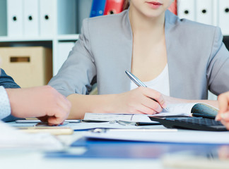  Business woman making notes at office workplace with hands of colleagues in the foreground. Only...