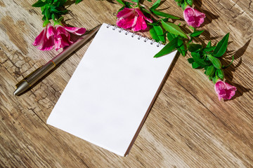 Naklejka na ściany i meble Mocap. Notepad with white paper and pen, decorated with a sprig of pink flowers on a plastic surface, simulated wood, 