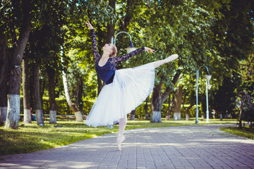 Young beautiful ballerina dancing against a background of city panorama in the park 