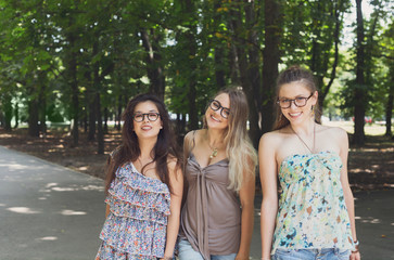 Three beautiful young boho chic stylish girls walking in park.