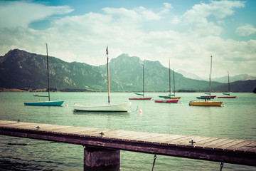 Small vintage sailboats anchoring. Alpine lake, landing stage and mountains.