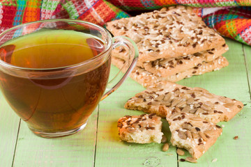 crispy bread with seeds of sunflower, flax and sesame seeds with a cup of tea on a green wooden background